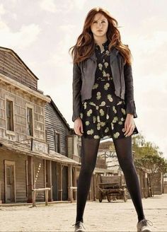 a woman is standing in front of an old house wearing tights and heels with her hands on her hips