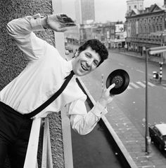 black and white photograph of a man holding a record in front of a city street