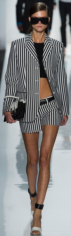 a woman walking down a runway wearing a black and white striped suit with sunglasses on her face