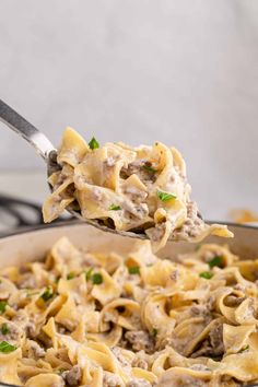 a spoon full of pasta with meat and cheese on it is being held over the skillet