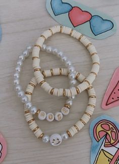 three bracelets with buttons and beads on top of a wooden table next to magnets