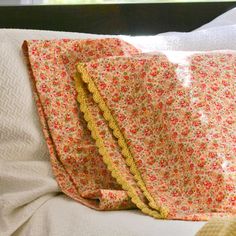 two pillows on top of a bed with white sheets and yellow ruffle trims