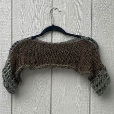 a knitted sweater hanging from a hook on a white wooden wall with wood slats in the background