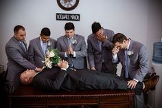 a group of men standing around a man laying on top of a table with flowers