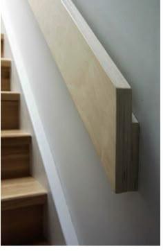 a wooden stair rail on the side of a white wall next to some wood steps