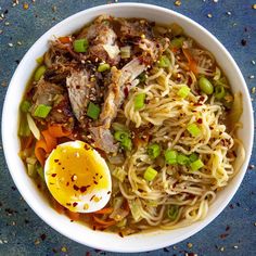 a white bowl filled with noodles, meat and veggies next to an egg