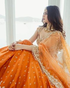 a woman in an orange and gold bridal gown sitting on a window sill