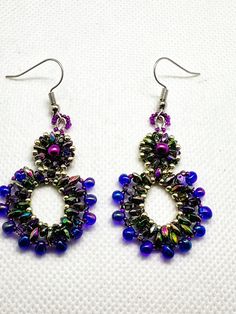 These beautiful, one of a kind, earrings were hand stitched using a variety of pink, purple, and silver Czech beads. They were created using pink pearls, iris super and mini duos, purple drops, and silver and purple seed beads. The result is a unique and festive pair of earrings that are perfect for a formal event or to dress up an everyday ensemble. They hang from hypo allergenic ear wires and come carded with stoppers Nickel-free Purple Beaded Round Earrings, Unique Purple Earrings With Dangling Beads, Handmade Purple Beaded Earrings, Handmade Teardrop Beaded Earrings For Parties, Handmade Pearl Drop Earrings For Party, Handmade Purple Chandelier Earrings As Gift, Elegant Handmade Iridescent Earrings, Handmade Iridescent Drop Earrings, Handmade Purple Dangle Hoop Earrings