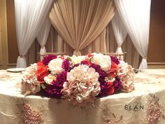 a round table with flowers on it in front of drapes and draperies at an event