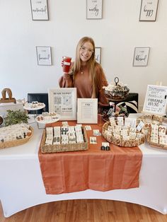 a woman standing behind a table filled with desserts and pastries, holding a cup