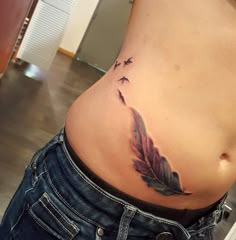 a woman's stomach with a feather tattoo on her belly and two birds flying in the sky