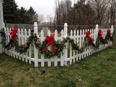 a white picket fence decorated with christmas wreaths and red bow ties on the top