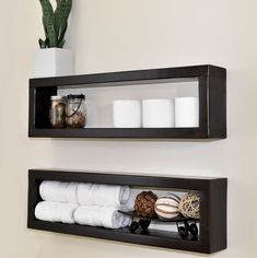 two black shelves holding towels, candles and other items in the bathroom on top of each shelf