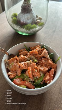 a bowl filled with food sitting on top of a wooden table next to a vase