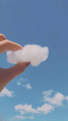 a hand holding cotton in front of a blue sky with white puffs on it