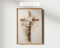 a cross with white flowers on it hanging in a wooden frame against a wall that says say grace print co