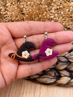 a person is holding two small earrings with flowers on the top and one has a witch's hat