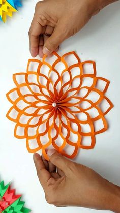 two hands are holding an origami flower on a white table with colorful paper flowers