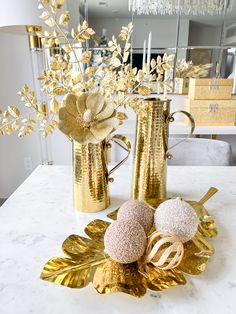 two gold vases sitting on top of a white table next to flowers and candles