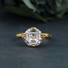 a close up of a diamond ring on a black surface with flowers in the background