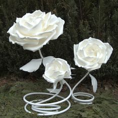 three white roses sitting on top of a metal object in front of some bushes and trees