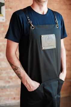 a man wearing an apron and holding his hands in his pockets while standing next to a brick wall