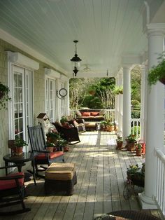 a porch with rocking chairs and potted plants on the front steps, surrounded by white pillars