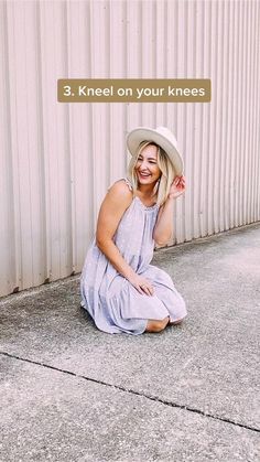 a woman sitting on the ground in front of a building wearing a hat and dress