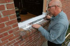 a man working on a window sill in front of a brick building