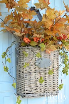 a wicker basket hanging on the front door with autumn leaves and berries in it