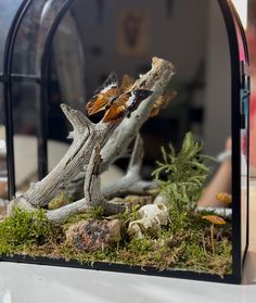 a close up of a fake tree with rocks and plants in it's display case