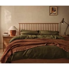 a bed with green sheets and pillows in a room next to a lamp on a table