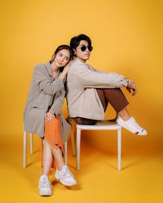 two people are sitting on a chair posing for a photo in front of a yellow background