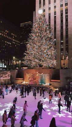 people skating on an ice rink in front of a large christmas tree with lit up lights