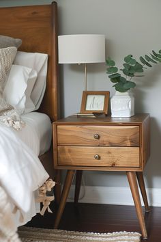 a nightstand with a plant on it next to a bed