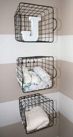 two metal baskets holding towels and blankets in the corner of a small room with striped walls