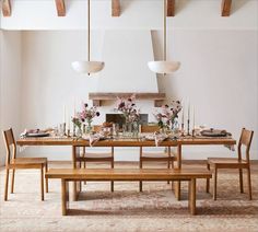 a dining room table with flowers and candles on it, along with two benches in front of the table