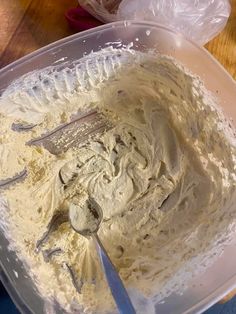 a mixing bowl filled with white batter on top of a wooden table next to a plastic container