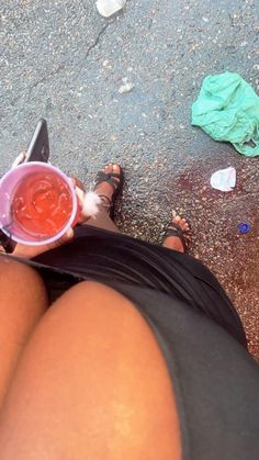 a woman sitting on the ground with her legs crossed holding a pink cup filled with liquid