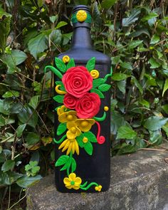 a black bottle with red and yellow flowers painted on it sitting in front of some bushes