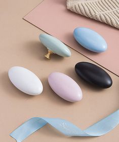 four different colored stones and a blue ribbon on a pink surface next to a pair of scissors