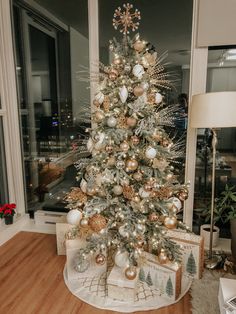 a white christmas tree with gold and silver ornaments in a living room next to a window