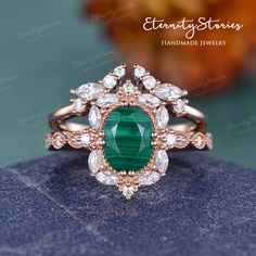 an emerald and diamond ring on top of a blue stone surface with leaves in the background