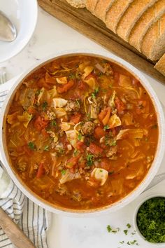 a white bowl filled with meat and vegetable soup next to sliced bread on a cutting board