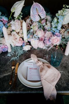 a place setting with pink and blue flowers on the table, along with silverware