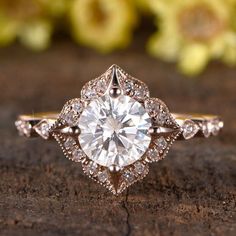 a close up view of a diamond ring on top of a piece of wood with flowers in the background