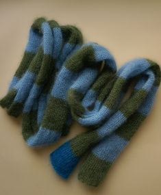 two blue and green knitted mittens laying next to each other on a table