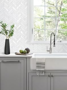 a white kitchen with gray cabinets and counter tops is pictured in this image, there are plants on the window sill next to the sink