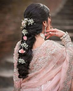 a woman with long black hair and flowers in her hair, wearing a pink sari