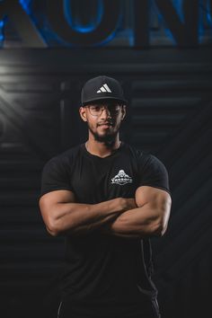 a man in black shirt and cap standing with his arms crossed